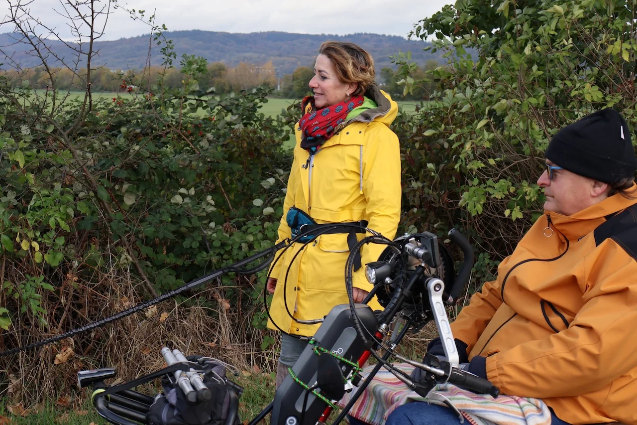 Odenwald - Stiftung Naturschutz - barrierefrei - zwei Personen im Freien, möglicherweise bereiten sie sich auf eine Freizeitaktivität wie Gleitschirmfliegen oder die Verwendung eines speziellen Mobilitätsgeräts vor.